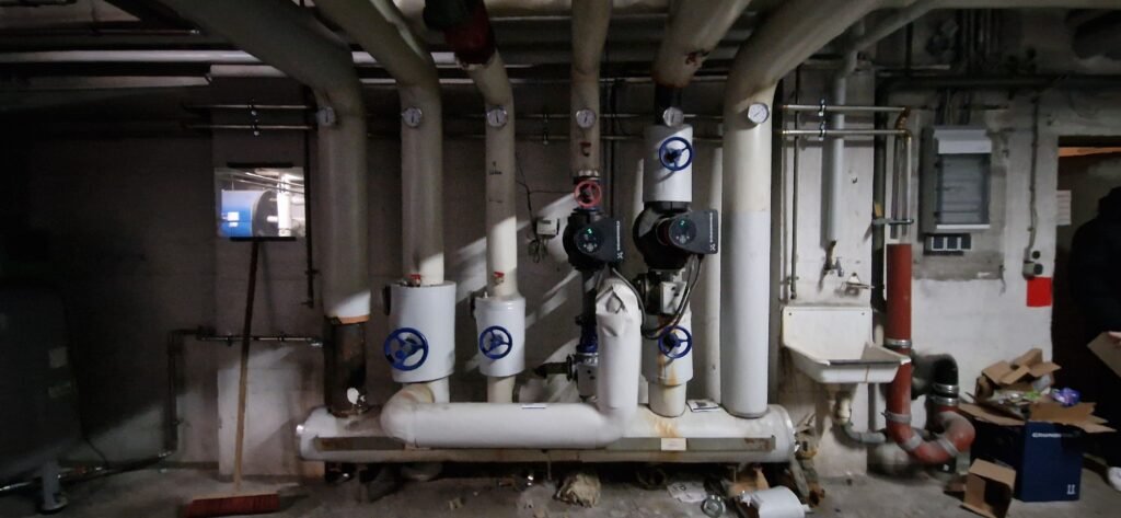 Technikzentrale eines Mehrfamilienhauses: Heizungsverteiler mit Umwälzpumpen und Absperrarmaturen